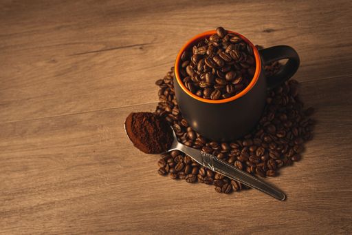 A closeup shot of coffee beans on a cup and spilled on a wooden surface