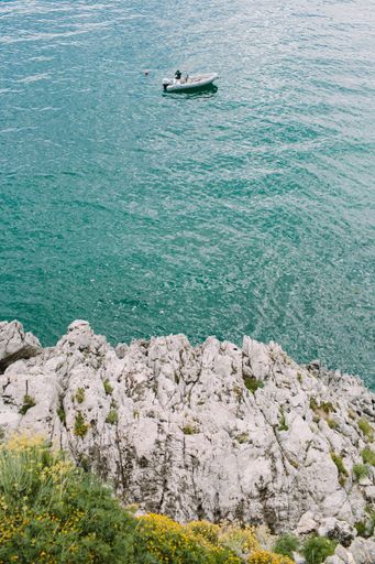A lone boat drifts on calm turquoise waters against a backdrop of rocky cliffs.