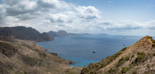 A view of a landscape with a sea, mountains, and white clouds