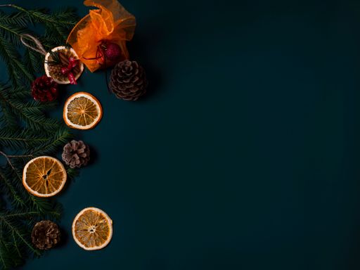 A top view of pine branches and cones with dried orange slices on a dark surface with space for text