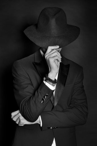 A secret adult mafia boss wearing a suit and covering his head with a fedora hat