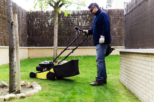 A large format shot of a gardener mowing the lawn and tending the garden