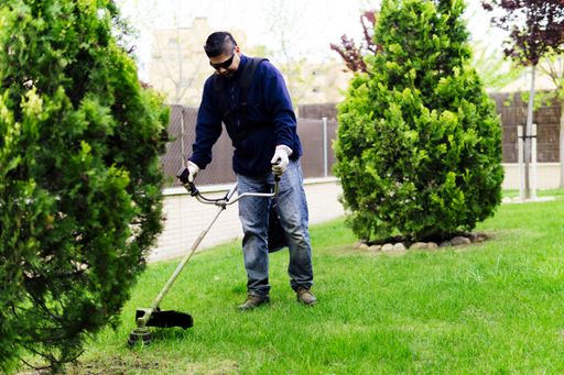 A large format shot of a gardener mowing the lawn and tending the garden