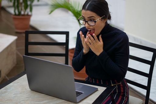A Hispanic woman looking shocked at her laptop after getting a promotion