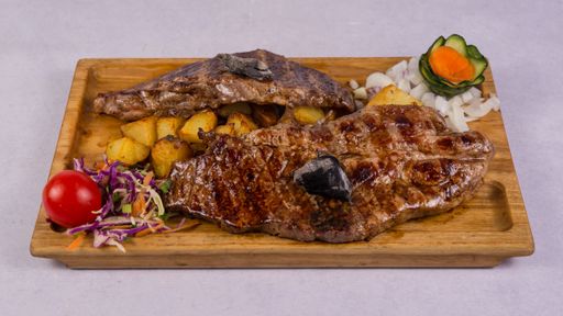 A view of grilled steaks with vegetables on a wooden plate isolated on a white background