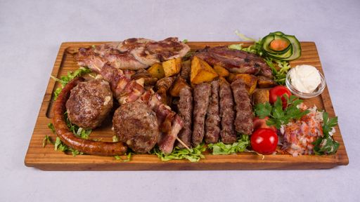 A view of grilled meat assortment with vegetables on a wooden plate isolated on a white background