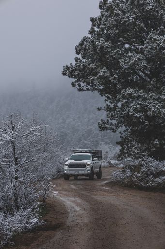A white truck camper driving through backroads in a winter forest in Colorado