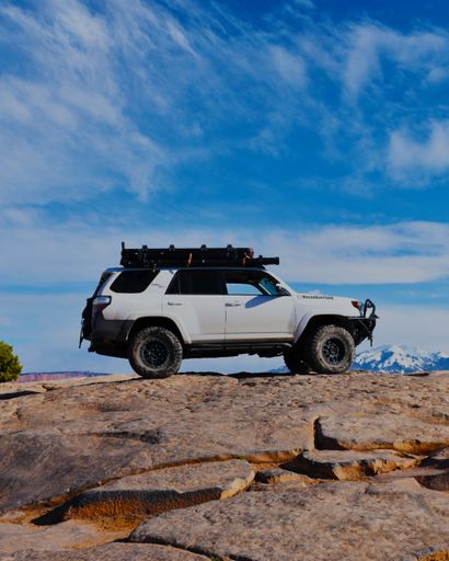 A vertical shot of a white 4runner off-road vehicle on the top of a hill in Moab, Utah