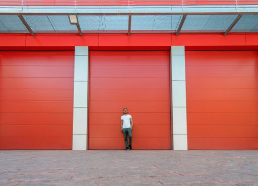 Man portrait leaning in the middle of a red warehouse door