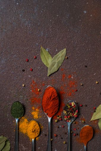 A top view of small spoons with red paprika, pepper and curry on isolated background