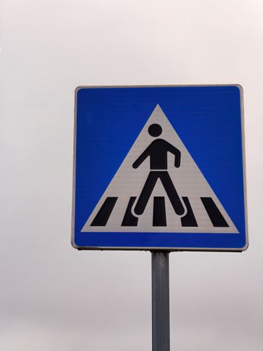 Vertical shot of a square pedestrian crossing sign attached on a pole against a blue sky