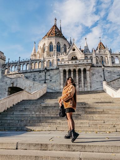 Portrait of beautiful young woman wearing stylish winter clothes, standing on stairs in front of Fisherman's bastion in Budapest, Hungary