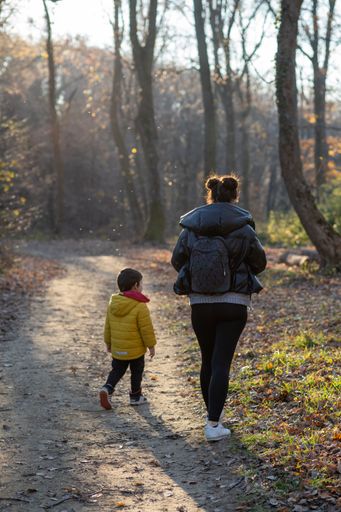 A vertical back view of a baby and his mother  walking along the path in the park on the cold winter day