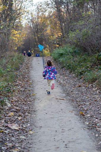 A vertical back view of a baby walking along the path in the park on the cold winter day