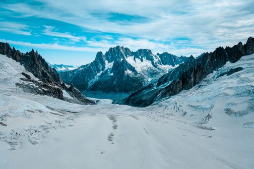 A beautiful shot of a snowy hill with mountains in the distance under a cloudy sky