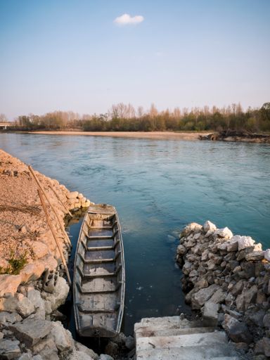 A vertical shot of an old wooden boat moored to a stone shore and a small stone cove on the river Drava, Croatia