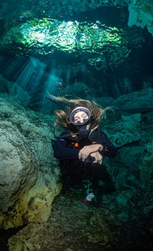 A vertical shot of a Caucasian woman with diving equipment under the water