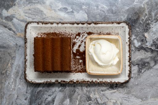 A plate of tiramisu and ice cream in a porcelain serving dish on a marble floor