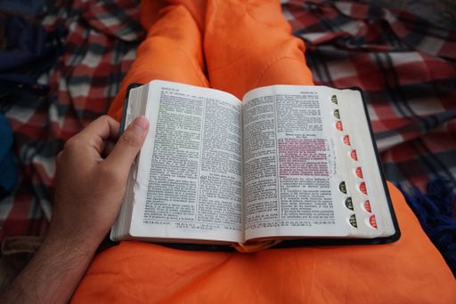 A close shot of a male holding an open book on his lap with a blurred background