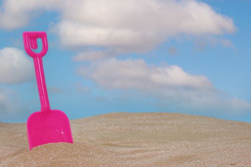 A closeup shot of the ocean pink sand shovel and the cloudy sky on the background