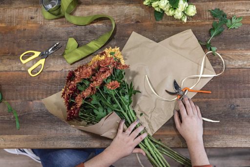 A top view of female hands creating a beautiful bouquet on a wooden table - businesswoman concept