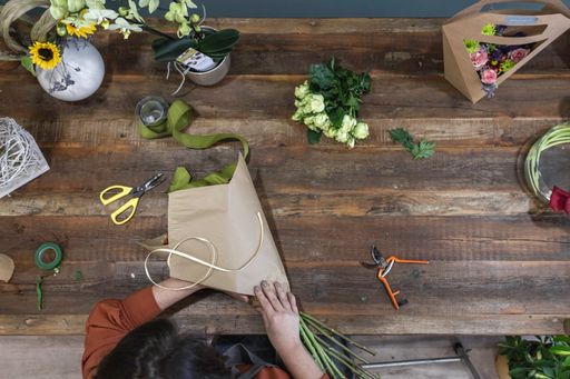 A top view of female hands creating a beautiful bouquet on a wooden table - businesswoman concept