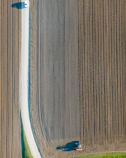 An aerial view of a tractor working in an agricultural field at sunset in Udine, Friuli Venezia Giulia, Italy