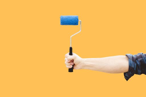 A vertical shot of a paint roller in the hand of a man, in a yellow background