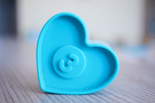 A closeup shot of a blue plastic heart-shaped toy with number three on a center