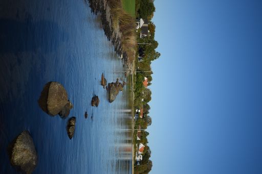 A vertical shot of some stones in the lake in the background of a townscape.
