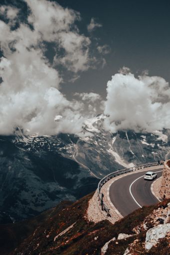 A vertical shot of a car driving on a highway under huge clouds