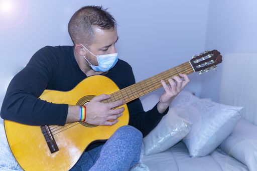 A closeup shot of a young male wearing medical face mask and playing guitar
