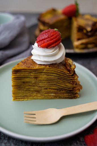 A vertical photo of a piece of pancake cake with whipped cream and strawberry topping