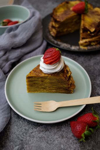 A vertical photo of a piece of pancake cake with whipped cream and strawberry topping