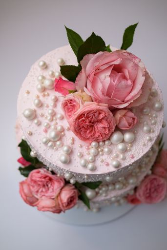 A vertical top view of a two-layer buttercream cake with edible pearls and roses