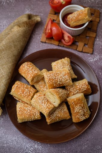A photo of a bread stick dipped in ketchup and tomato slices, and bread sticks on a platter