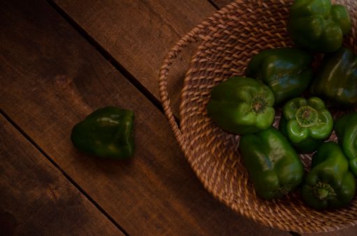 The top view of the green bell peppers on a wicker tray and wooden floor