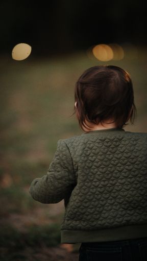 A selective focus shot of a toddler baby girl from behind walking in the park holding her mom's hand