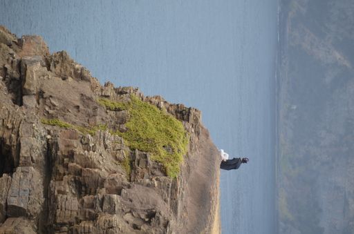 A vertical shot of a man sitting on the edge of a rocky cliff