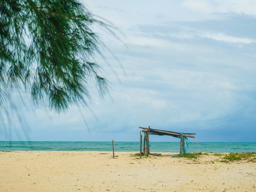 A scenic view of a sandy beach with wooden structure and a calm sea with a light cloudy sky in the background