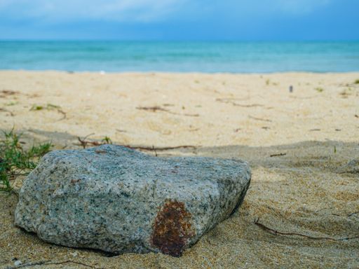 A body of water near the sand beach and a rock under a bright sunlight
