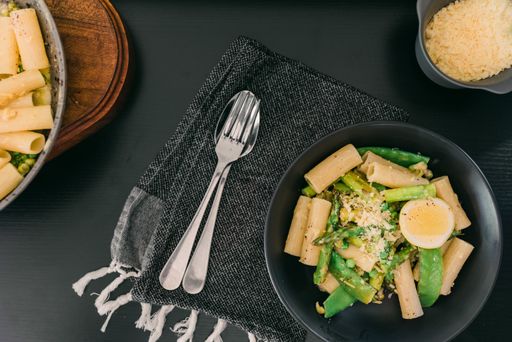 A plate with pasta asparagus and egg on a black table