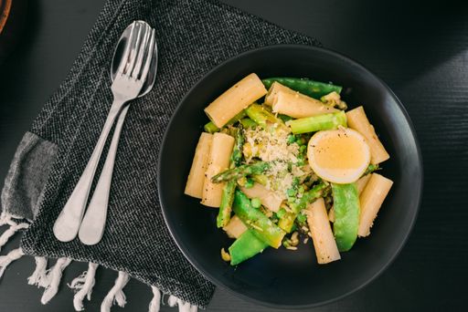 A plate with pasta asparagus and egg on a black table