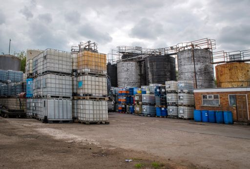 Storage tanks, barrels and drums of chemical waste in compound at waste treatment and disposal facility.