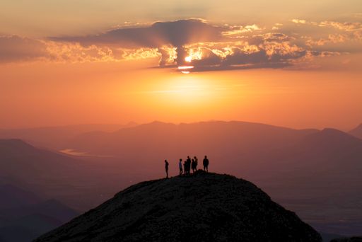 A silhouette view of a group of people standing on a mountain peak watching an epic sunset