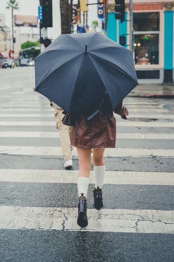 A vertical shot of the young woman walking down a wet street with an umbrella on a rainy day