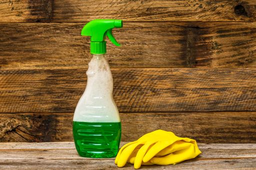 A closeup shot of a cleaning sprayer and rubber gloves on a wooden table