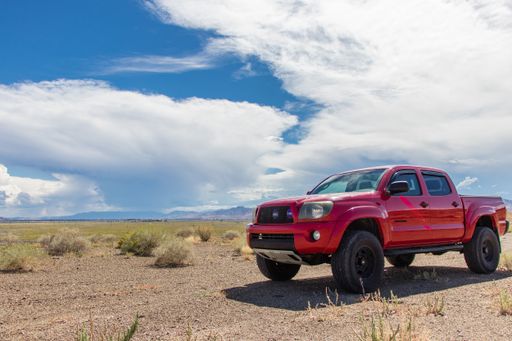 A scenic view of a red car in a rural area on cloudy sky background