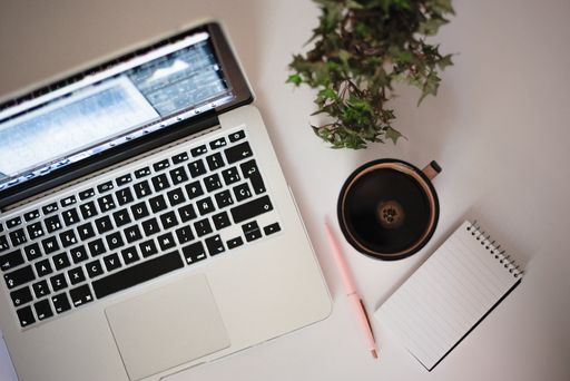 A high angle shot of laptop, cup of coffee, notebook, pen and plant isolated on white background
