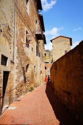 A vertical shot of a narrow alley surrounded by old stone building in San Gimignano